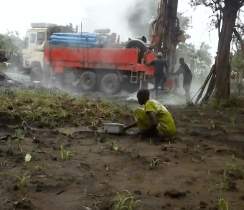 Refugee scoops water from ditch while borehole is being drilled. Nyumazi Camp, Uganda.